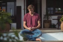 Hombre sentado en el porche y el uso de teléfono móvil en casa - foto de stock