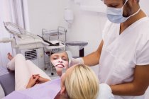 Стоматолог держит зеркало перед лицом пациента в клинике — стоковое фото