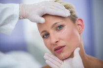 Médico examinando rosto paciente feminino para tratamento cosmético na clínica — Fotografia de Stock