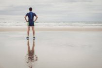 Vue arrière de l'athlète debout avec les mains sur les hanches sur la plage — Photo de stock