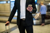 Parte média do empresário que usa o telefone móvel na área de espera no terminal do aeroporto — Fotografia de Stock