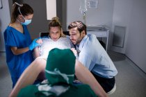 Врач осматривает беременную женщину во время родов, пока мужчина держит ее за руку в операционной — стоковое фото