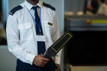 Partie médiane de l'agent de sûreté de l'aéroport tenant un détecteur de métaux dans l'aérogare — Photo de stock