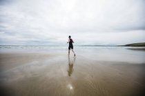 Visão traseira do homem em traje de natação e touca de natação correndo na praia — Fotografia de Stock
