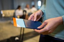 Mid-section of female passenger holding passport and boarding pass at airport terminal — Stock Photo