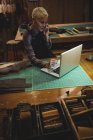 Handwerker benutzt Laptop beim Handy-Gespräch in Werkstatt — Stockfoto