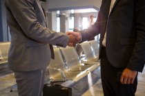 Mid-section of business people shaking hands in airport terminal — Stock Photo