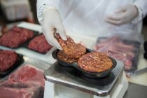 Primer plano del carnicero que pesa empanadas de carne a escala en la fábrica de carne - foto de stock