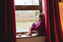 Menina pensativo sentado no peitoril da janela em casa — Fotografia de Stock