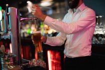 Seção intermediária do bartender que enche a cerveja da bomba da barra no balcão da barra — Fotografia de Stock