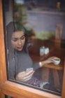 Красива жінка використовує мобільний телефон, маючи чашку кави в кафе — стокове фото