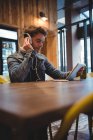 Человек слушает музыку с наушниками при использовании цифрового планшета в кафе — стоковое фото