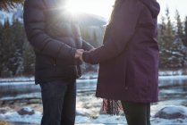 Mid section of romantic couple standing by river in winter — Stock Photo