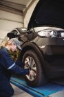 Жінка-механік, що вивчає автомобільне колесо в ремонті гаража — стокове фото
