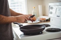 Средняя часть человека разбивает яйцо в сковородке на кухне дома — стоковое фото