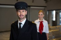 Retrato de piloto feliz y azafata de pie en la terminal del aeropuerto - foto de stock