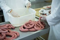 Corte médio de açougueiros que processam salsichas em fábrica de carne — Fotografia de Stock