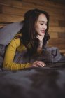 Улыбающаяся женщина лежит на кровати с помощью ноутбука в спальне дома — стоковое фото