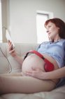 Беременная женщина с наушниками на животе расслабляется на диване в гостиной — стоковое фото