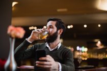 Uomo che tiene il cellulare e beve qualcosa al bar — Foto stock