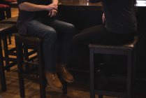 Section basse du couple assis sur des tabourets au comptoir du bar — Photo de stock