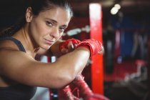 Портрет уверенной женщины-боксера, опирающейся на боксерское кольцо в фитнес-студии — стоковое фото
