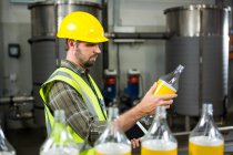 Вид збоку серйозного працівника чоловічої статі, який оглядає пляшки на заводі соків — стокове фото