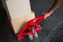 Mano ritagliata di lavoratore tirando carrello caricato con scatole in magazzino — Foto stock