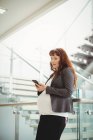Embarazada mujer de negocios utilizando el teléfono móvil cerca de la escalera en la oficina - foto de stock