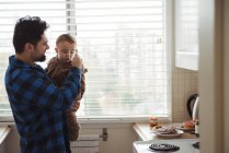 Отец и его ребенок пользуются мобильным телефоном на кухне — стоковое фото