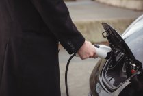 Partie médiane de l'homme chargeant la voiture électrique à la station de recharge du véhicule électrique — Photo de stock