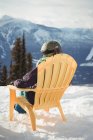 Vista trasera de la mujer sentada en la silla en la montaña cubierta de nieve contra el cielo - foto de stock