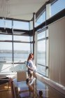 Mujer embarazada reflexiva mirando por la ventana en la sala de estar en casa - foto de stock