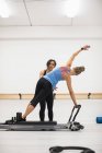 Entrenadora mujer que ayuda a la mujer con el ejercicio de estiramiento en reformador en el gimnasio - foto de stock