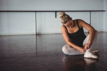 Ballerina adjusting stockings while sitting in ballet studio — Stock Photo
