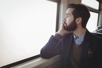 Homme d'affaires réfléchi regardant par la fenêtre dans le train — Photo de stock