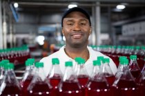 Primer retrato de un empleado masculino sonriente parado junto a botellas de jugo en fábrica - foto de stock