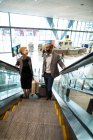 Business people interacting with each other while going up on escalator at airport terminal — Stock Photo