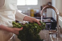 Media sezione di donna che lava i broccoli sotto il lavandino in cucina a casa — Foto stock
