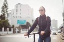 Woman in sunglasses riding a bicycle on city road — Stock Photo