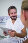 Doctor holding digital tablet while talking with patient at clinic — Stock Photo