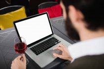 Homem usando laptop enquanto toma um copo de vinho no bar — Fotografia de Stock
