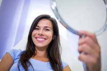 Portrait of smiling patient holding mirror at clinic — Stock Photo