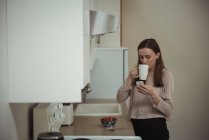 Жінка, дивлячись на мобільний телефон, маючи Кава у кухні в домашніх умовах — стокове фото