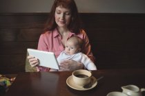 Mãe com bebê filha usando tablet digital no café — Fotografia de Stock