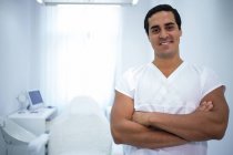Портрет чоловіка-стоматолога, що стоїть на руках, схрещених у стоматологічній клініці — стокове фото