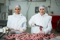 Portrait of smiling female butchers cutting sausages — Stock Photo
