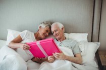 Seniorin überreicht Geschenk an Seniorin auf Bett im Schlafzimmer — Stockfoto