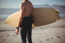 Mid-section of surfer standing with surfboard on beach — Stock Photo