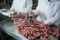 Close-up de açougueiros segurando salsichas na fábrica de carne — Fotografia de Stock